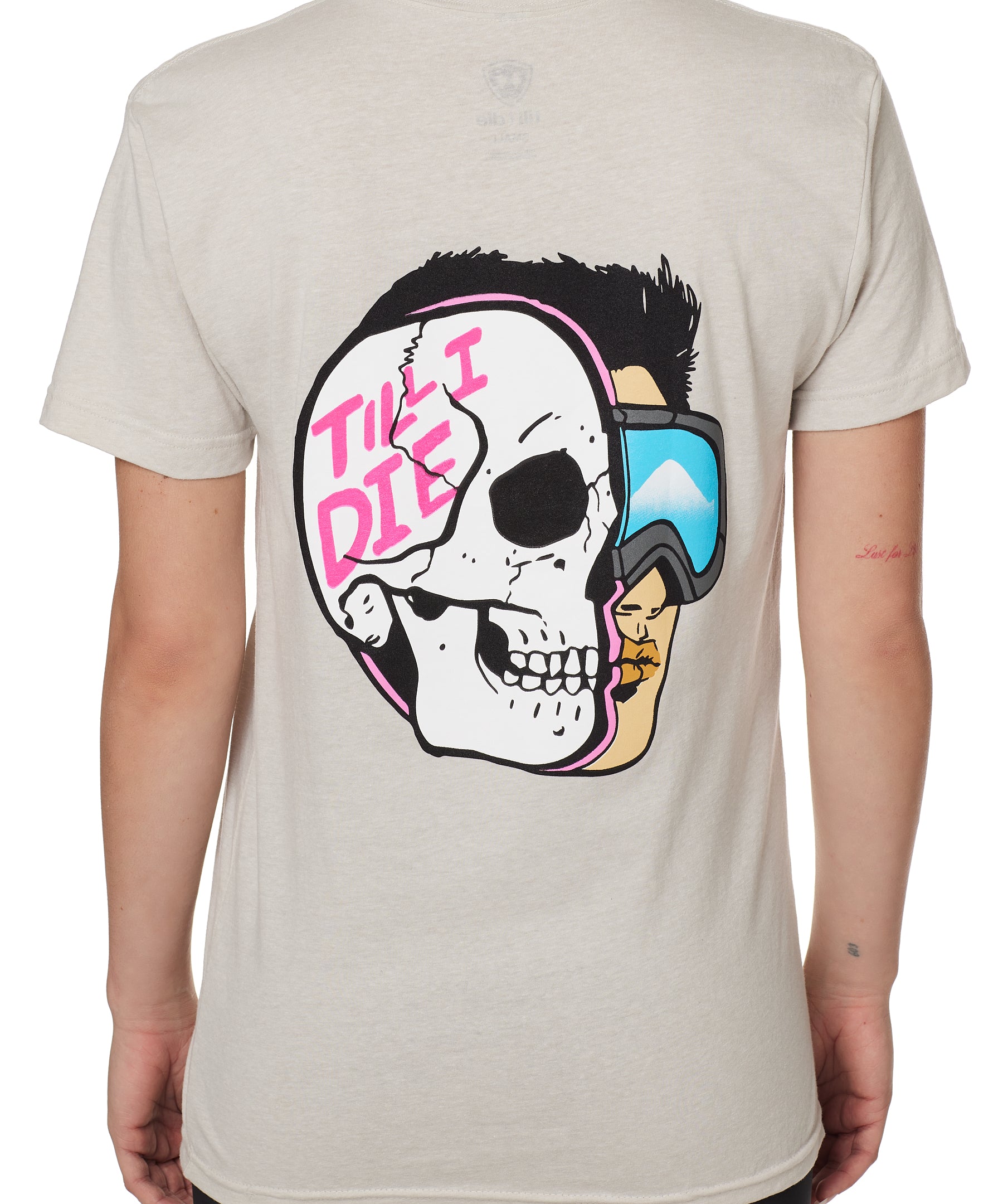 BACK OF A FEMALE MODEL WEARING A TAN TEE SHIRT WITH A GRPHIC OF A HALF SKULL HALF SKIER AND THE WORDS TILL I DIE
