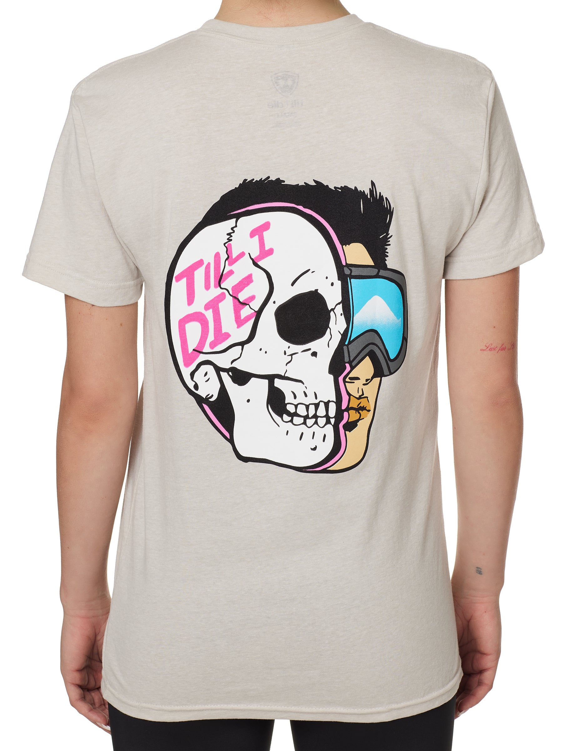 BACK OF A FEMALE MODEL WEARING A TAN TEE SHIRT WITH A GRPHIC OF A HALF SKULL HALF SKIER AND THE WORDS TILL I DIE