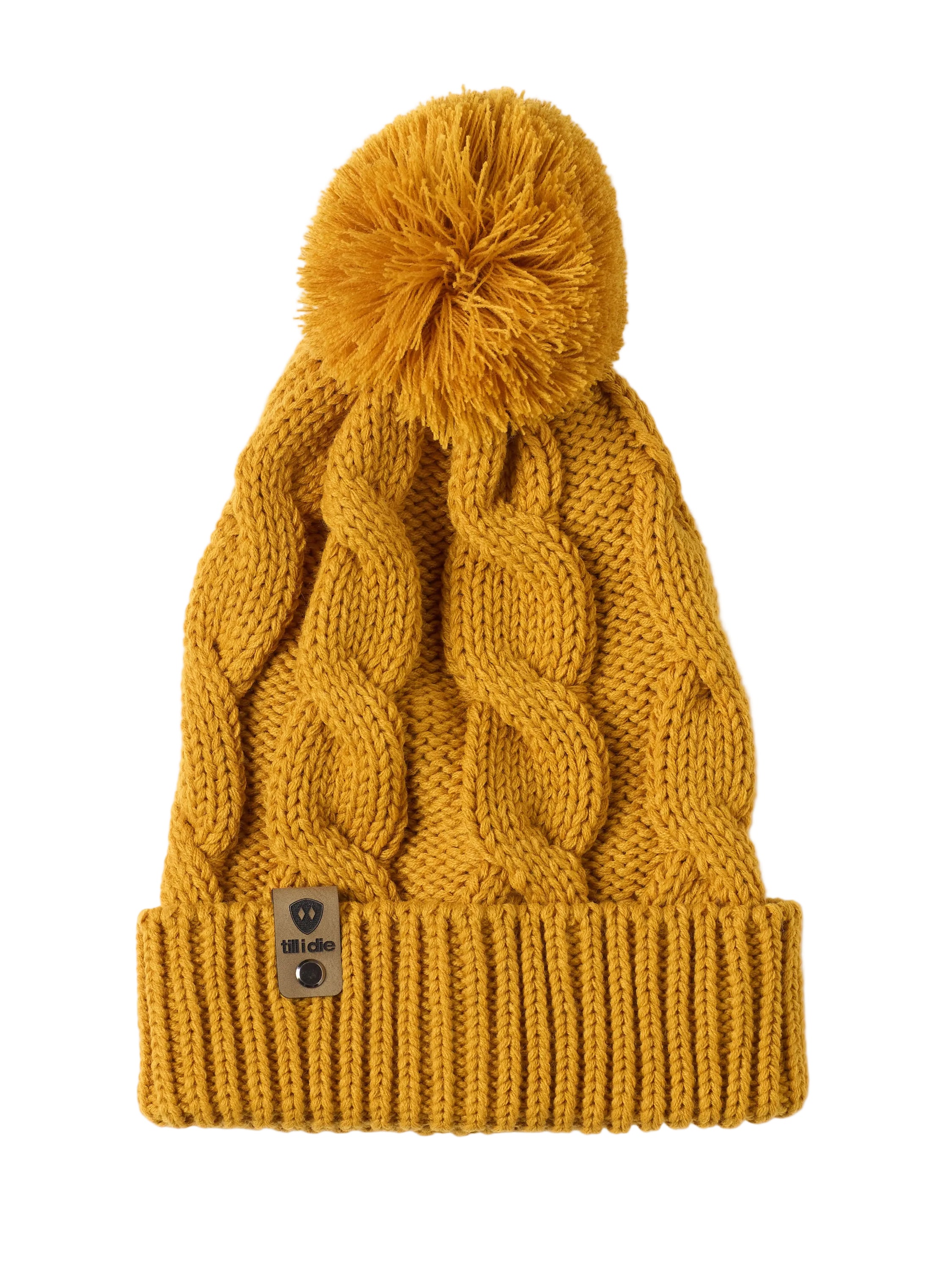 A mustard cable-knit beanie hat with a matching pom-pom on top and a ribbed cuff featuring a Till I Die Logo leather tab, shown against a plain white background.