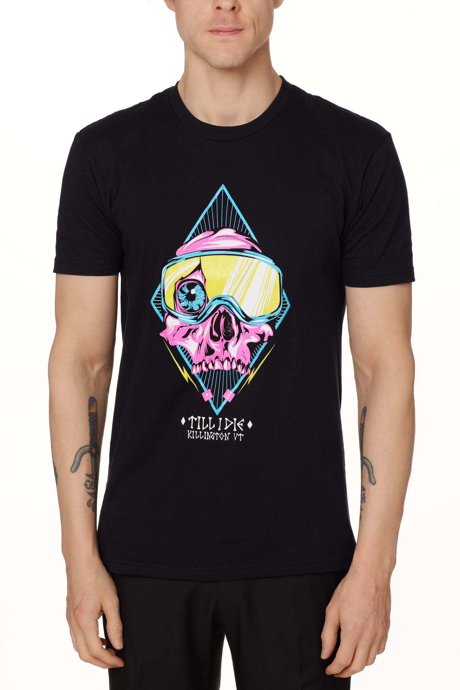 Front view of a male model wearing the Lucky 13 crew neck tee in black. The graphic features a pink skull with a cracked goggle lens revealing a wide eye, layered over a blue geometric pattern and yellow lightning bolts. “Till I Die” and “Killington, VT” text sit below the artwork.