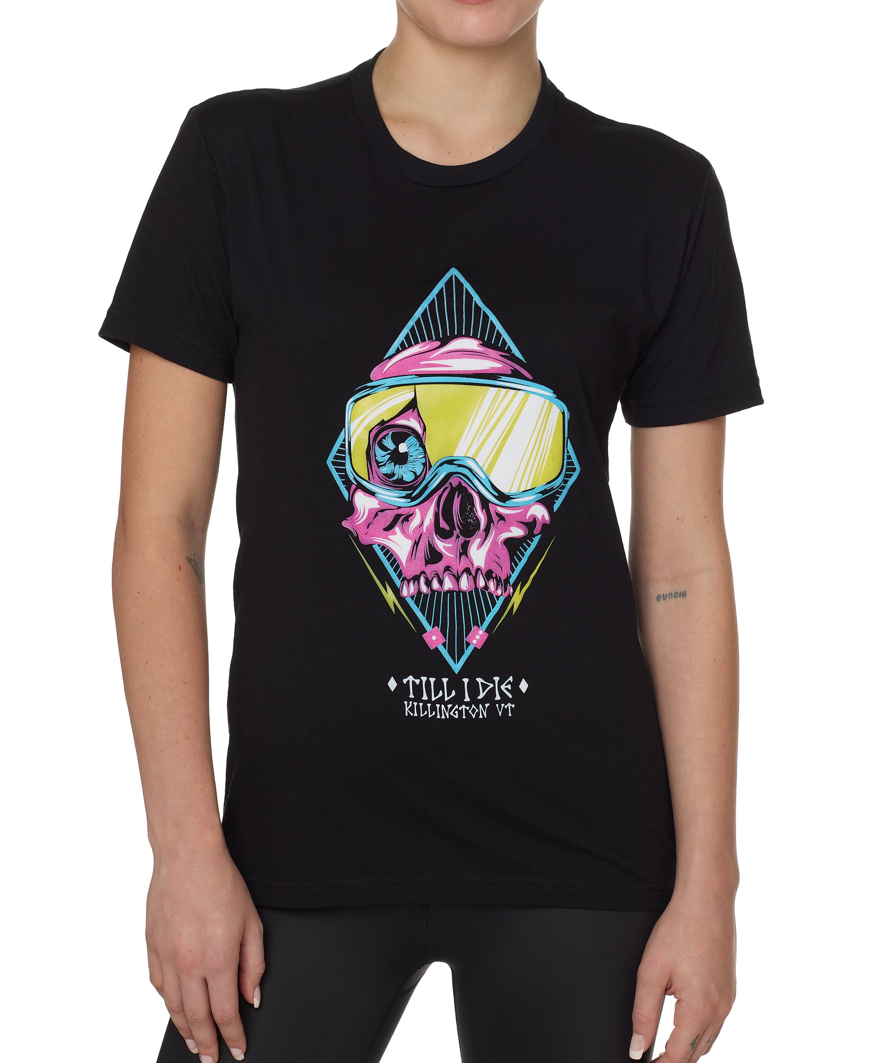 Front view of a female model wearing the Lucky 13 crew neck tee in black. The graphic features a pink skull with a cracked goggle lens revealing a wide eye, layered over a blue geometric pattern and yellow lightning bolts. “Till I Die” and “Killington, VT” text sit below the artwork.