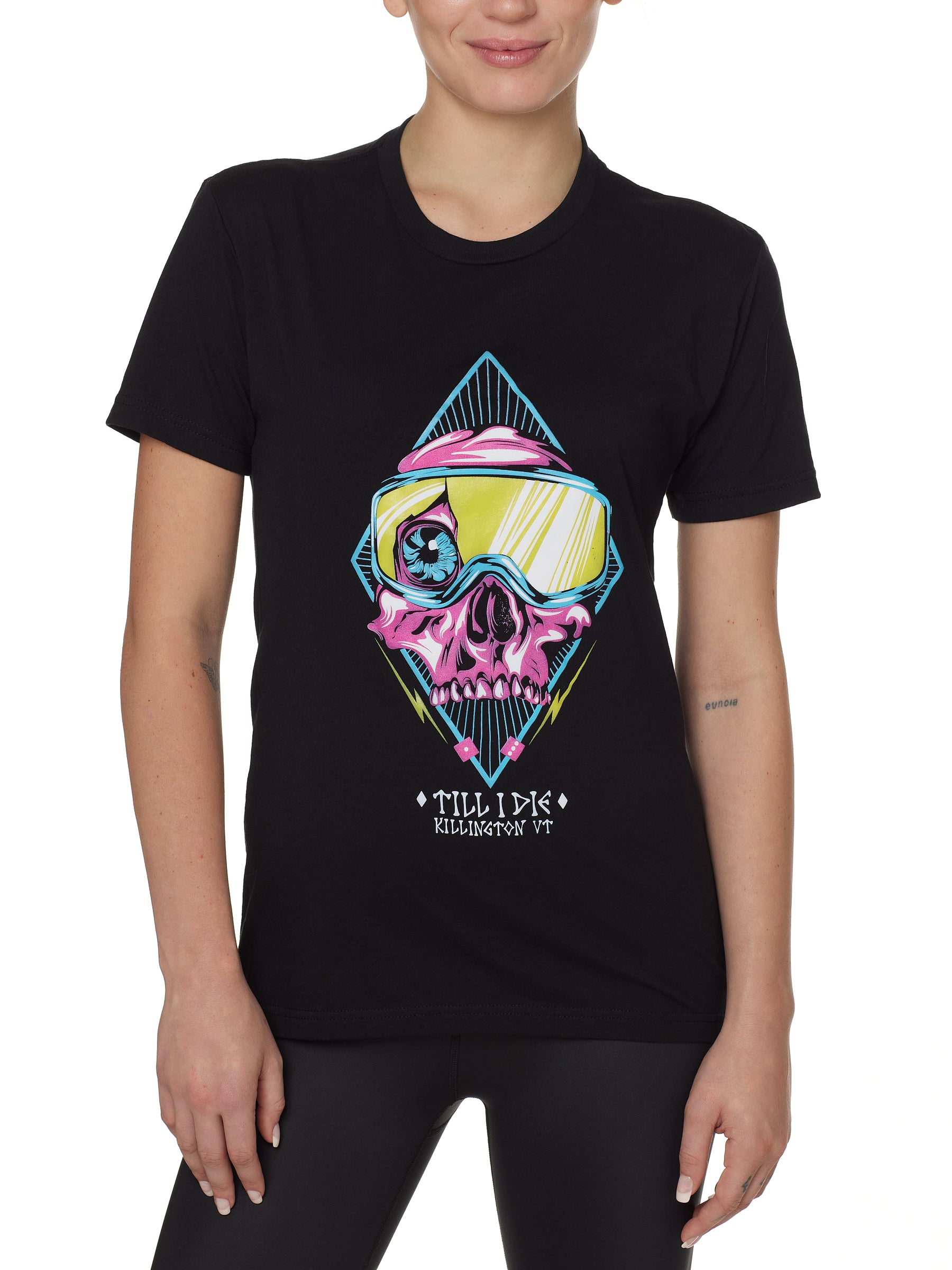 Front view of a female model wearing the Lucky 13 crew neck tee in black. The graphic features a pink skull with a cracked goggle lens revealing a wide eye, layered over a blue geometric pattern and yellow lightning bolts. “Till I Die” and “Killington, VT” text sit below the artwork.
