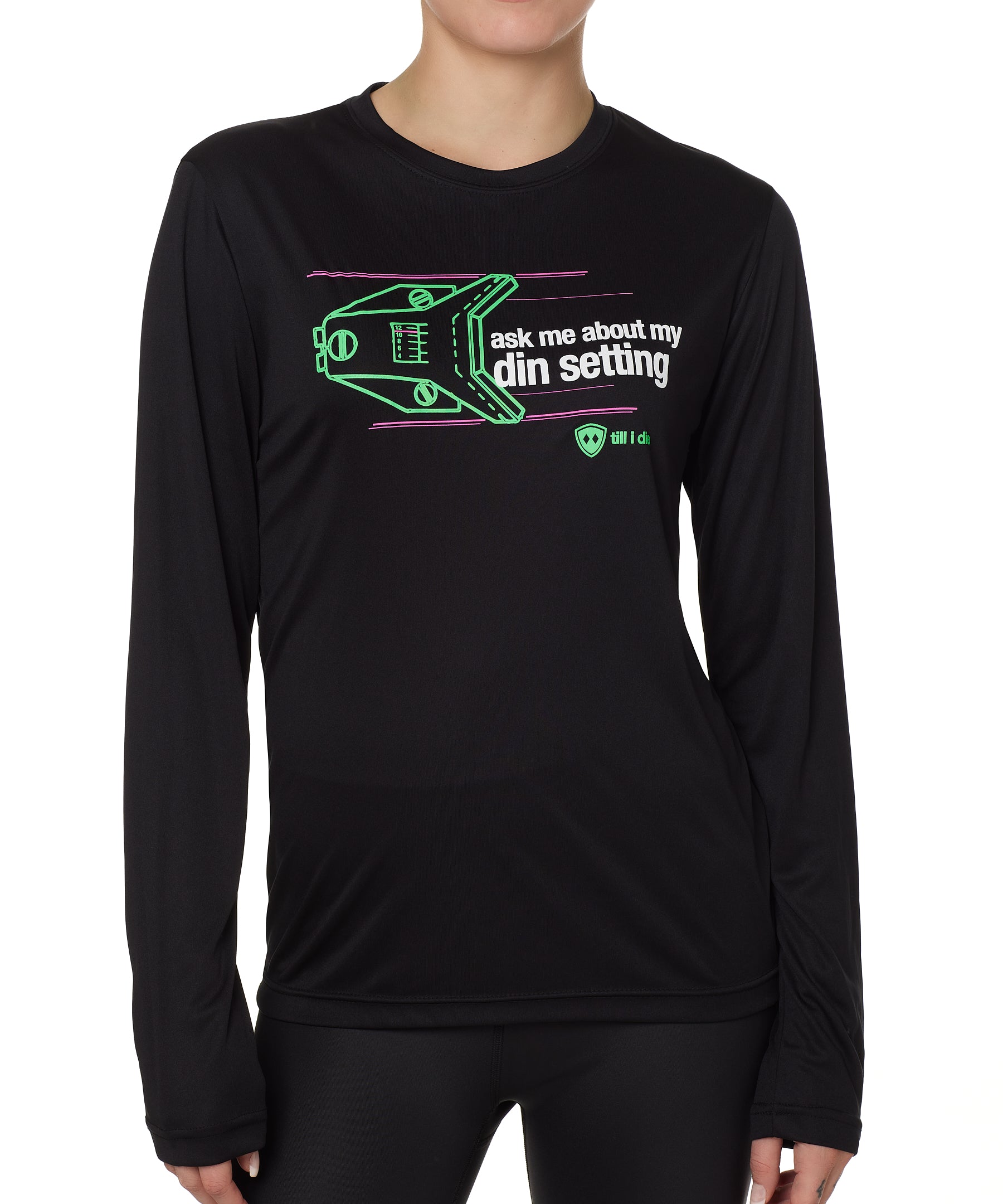 FEMALE MODEL WEARING A BLACK LONG SLEEVE PERFORMANCE SHIRT WITH A GRAPHIC OF A SKI BINDING TUNED TO 11 WITH THE WORDS "ASK ME ABOUT MY DIN SETTING"