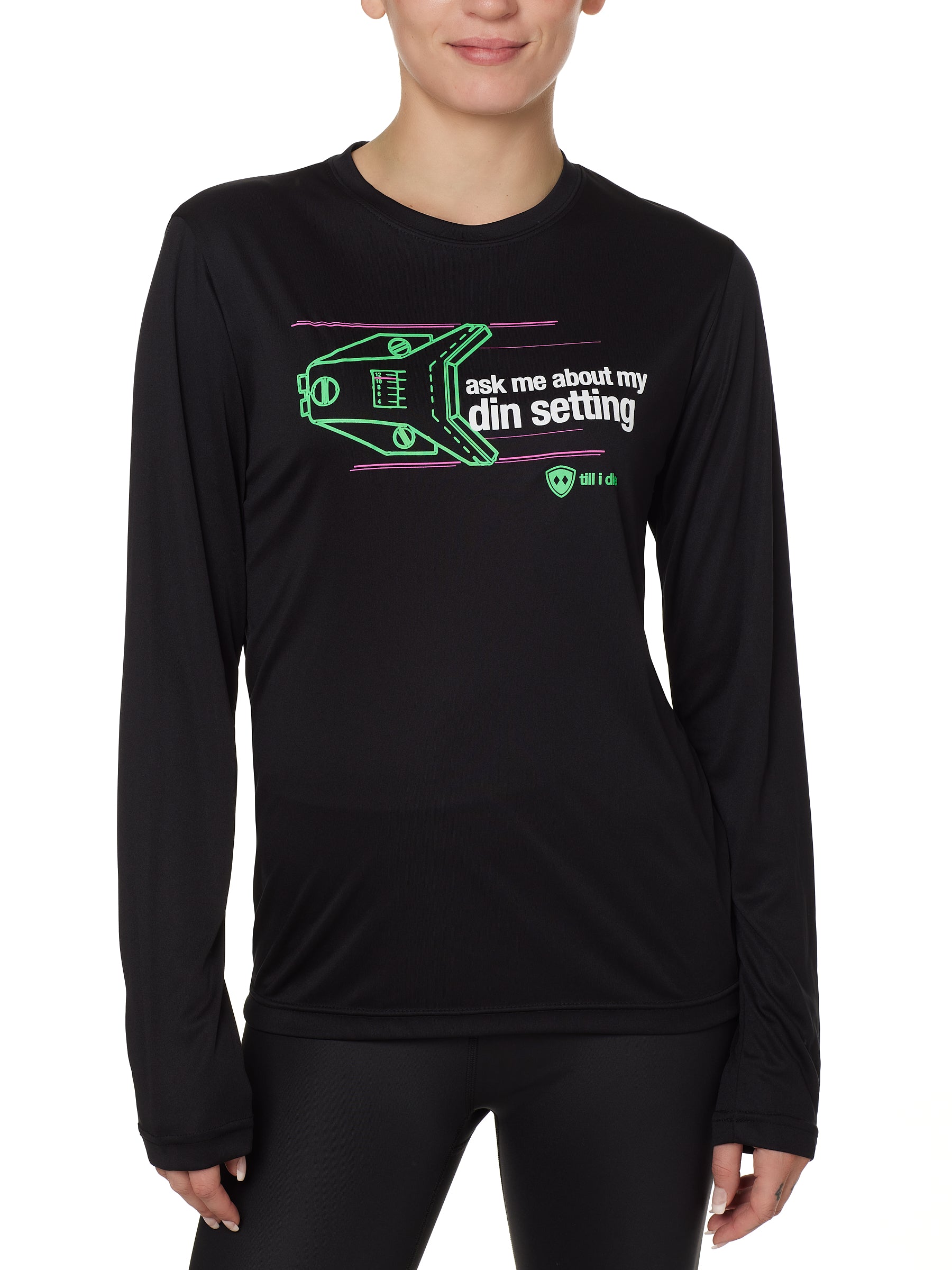 FEMALE MODEL WEARING A BLACK LONG SLEEVE PERFORMANCE SHIRT WITH A GRAPHIC OF A SKI BINDING TUNED TO 11 WITH THE WORDS "ASK ME ABOUT MY DIN SETTING"