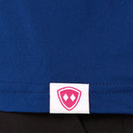 Close-up detail of a pink Double Diamond Shield woven hem label on a blue performance long sleeve shirt.