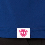 Close-up detail of a pink Double Diamond Shield woven hem label on a blue performance long sleeve shirt.