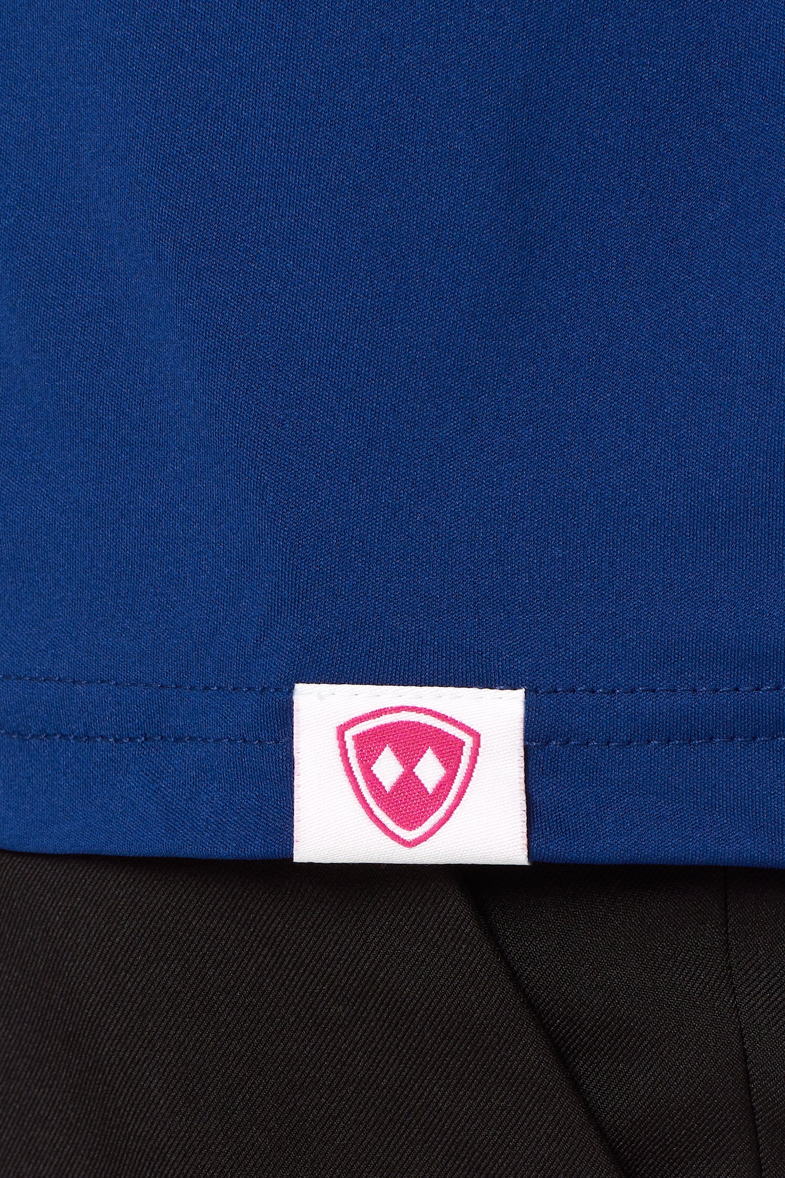 Close-up detail of a pink Double Diamond Shield woven hem label on a blue performance long sleeve shirt.
