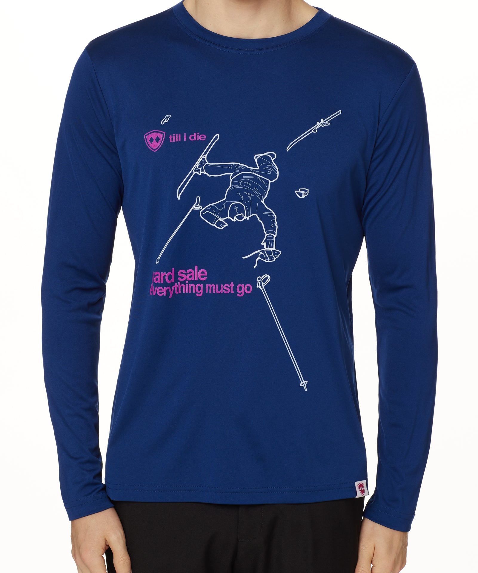 Front view of a male model wearing the Legends Yard Sale performance long sleeve shirt in blue. The graphic features a line art illustration of a skier sprawled in the snow, surrounded by scattered gear—gloves, skis, hat, and poles. Below the scene is the text: “Yard Sale – Everything Must Go.”