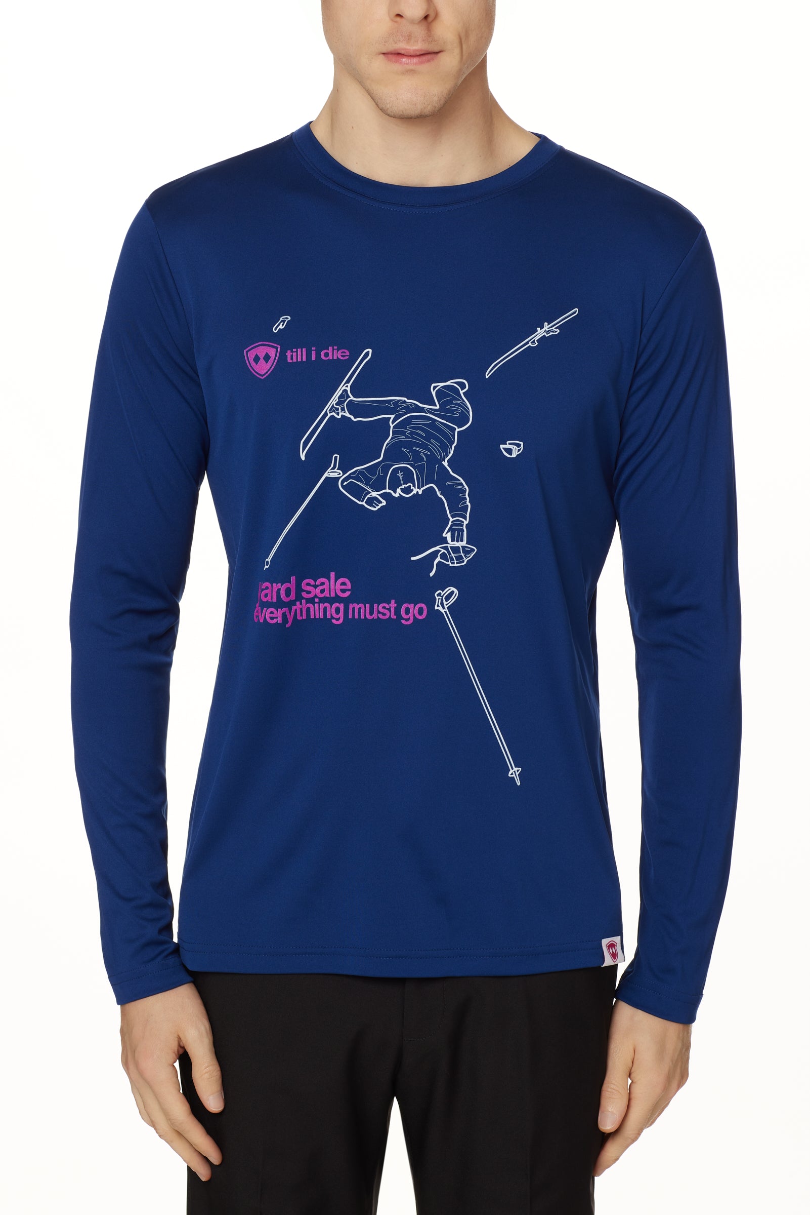 Front view of a male model wearing the Legends Yard Sale performance long sleeve shirt in blue. The graphic features a line art illustration of a skier sprawled in the snow, surrounded by scattered gear—gloves, skis, hat, and poles. Below the scene is the text: “Yard Sale – Everything Must Go.”