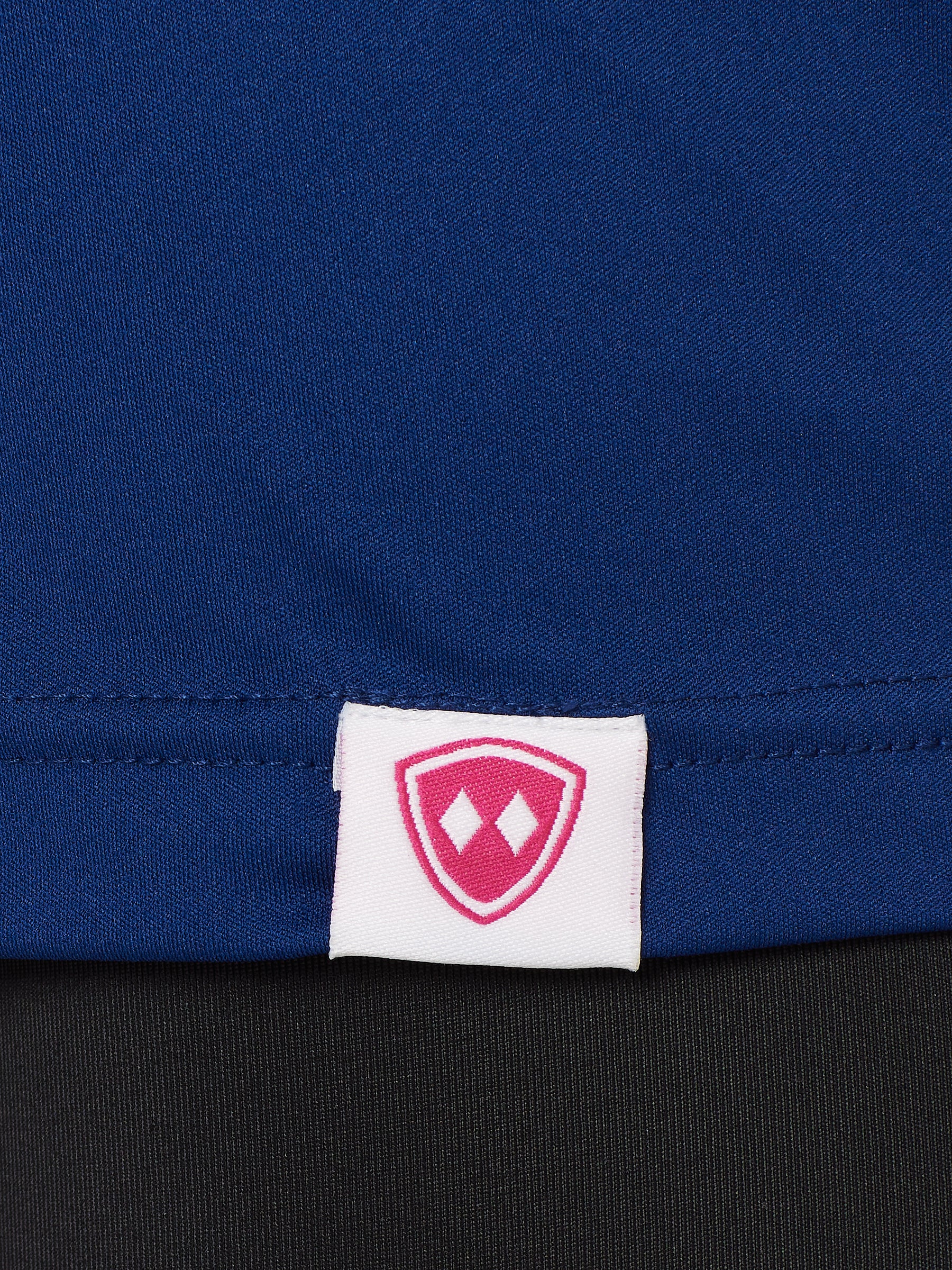 DETAIL OF A BLUE PERFORMANCE SHIRT WITH THE TILL I DIE LOGO HEM TAG