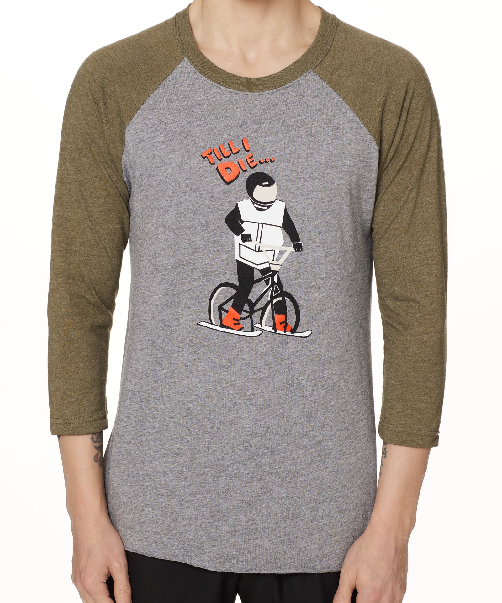 Front view of a male model wearing the Two Dollars Raglan 3/4 sleeve tee. The shirt features military green sleeves and a heather gray body, with a graphic of a ski biker in a full-face helmet. Above the illustration is “Till I Die…” text.