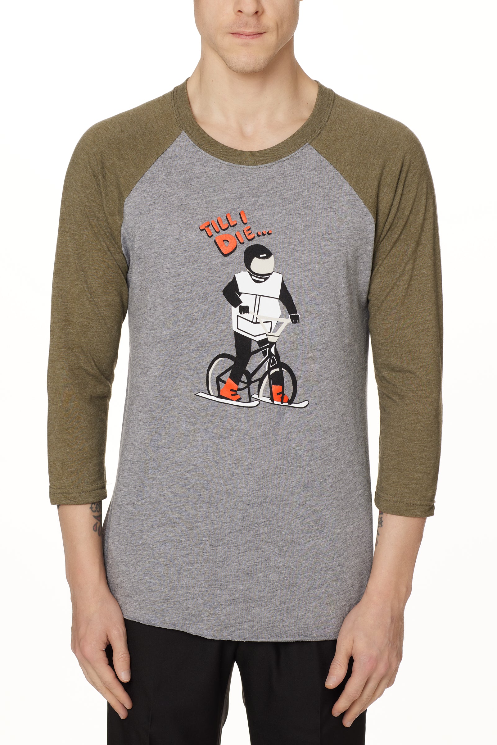 Front view of a male model wearing the Two Dollars Raglan 3/4 sleeve tee. The shirt features military green sleeves and a heather gray body, with a graphic of a ski biker in a full-face helmet. Above the illustration is “Till I Die…” text.