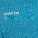DETAIL OF A HEATHER TEAL HOODIE WITH THE WORDS "DO WHAT YOU LOVE. DO IT FOREVER." EMBROIDERED IN WHITE AND TEAL