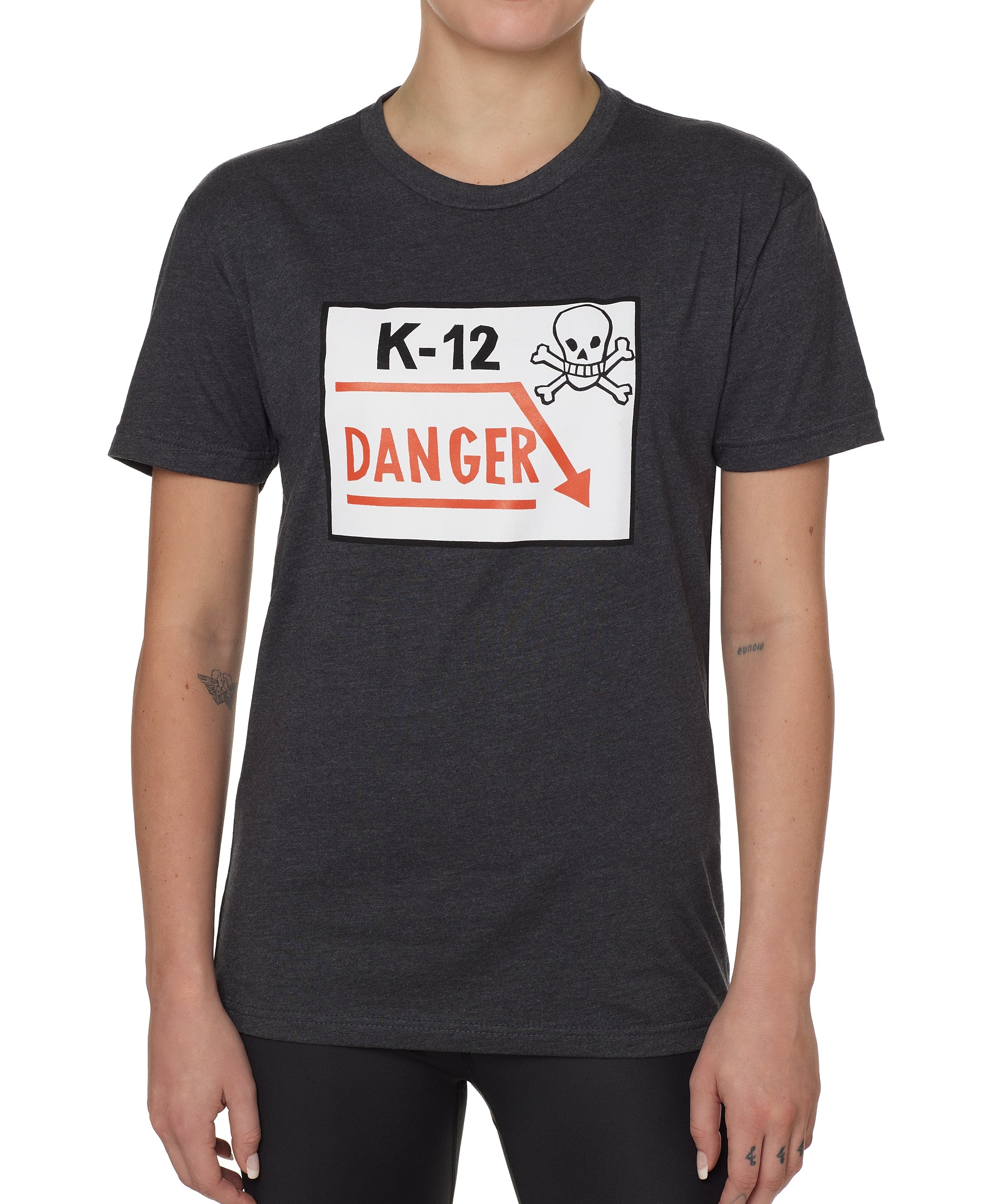 Front view of a female model wearing a gray short-sleeve t-shirt featuring a “K-12 Danger” graphic with a bold skull and crossbones design.