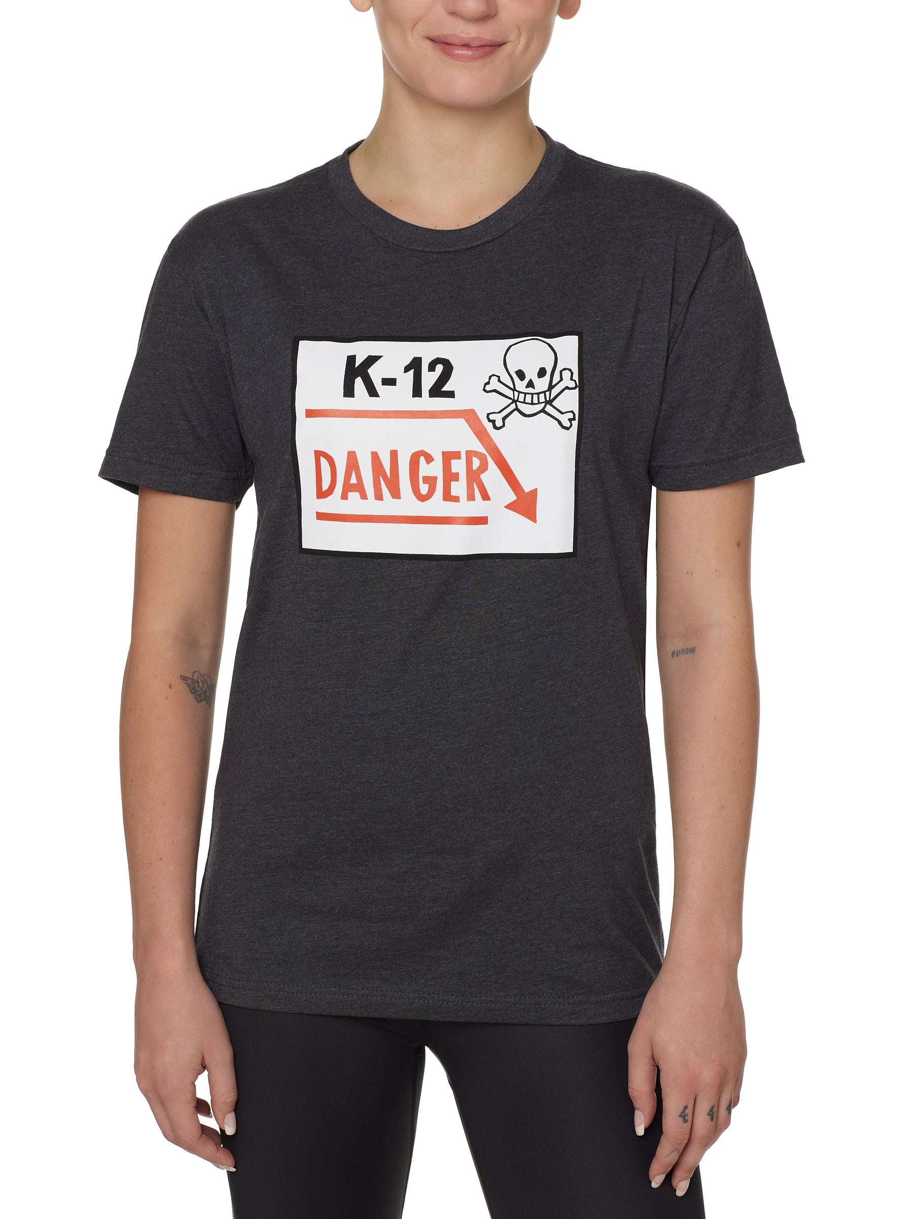 Front view of a female model wearing a gray short-sleeve t-shirt featuring a “K-12 Danger” graphic with a bold skull and crossbones design.