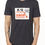 Front view of a male model wearing a gray short-sleeve t-shirt featuring a “K-12 Danger” graphic with a bold skull and crossbones design.