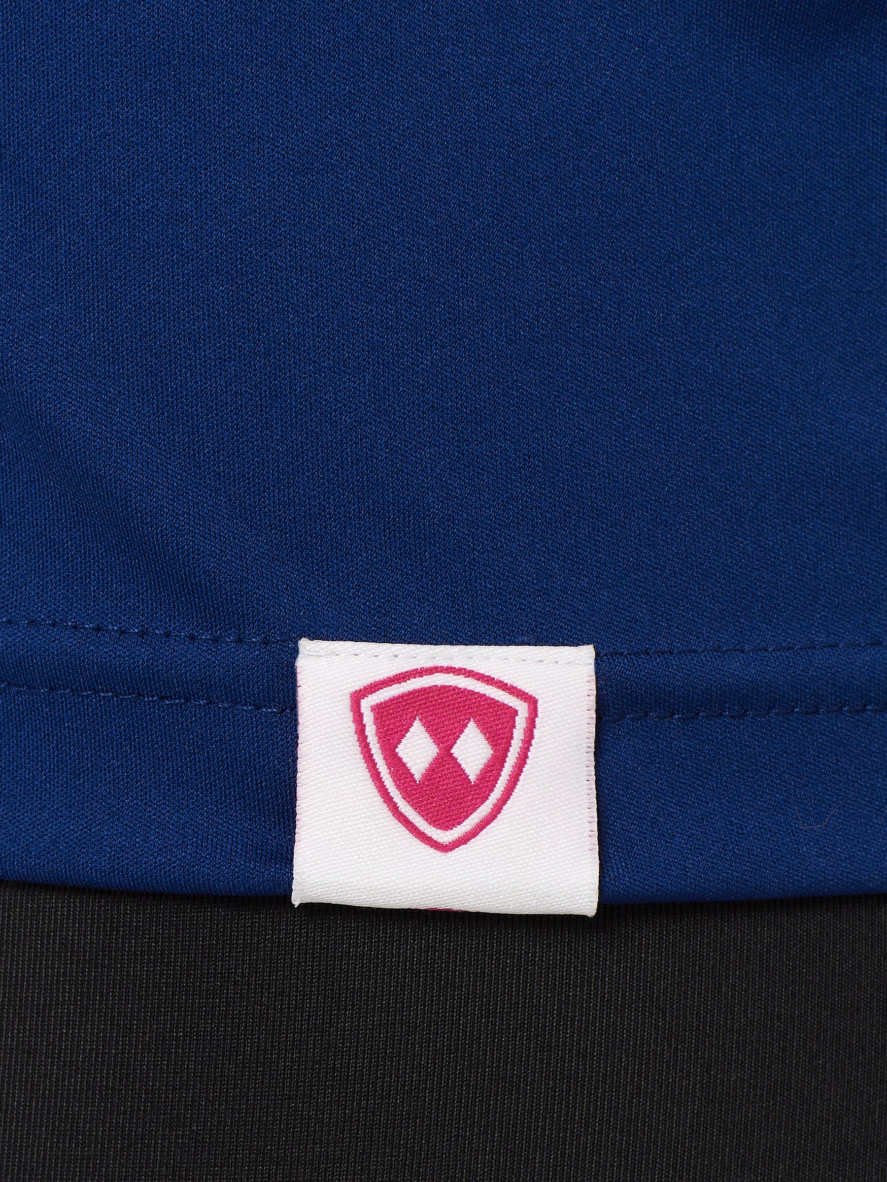 DETAIL OF A BLUE PERFORMANCE SHIRT WITH THE TILL I DIE SHIELD LOGO ON A WOVEN HEM TAG
