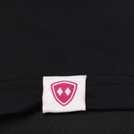 Close-up detail of a pink Double Diamond Shield woven hem label on a black performance long sleeve shirt.