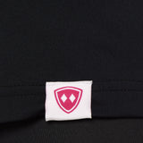 Close-up detail of a pink Double Diamond Shield woven hem label on a black performance long sleeve shirt.