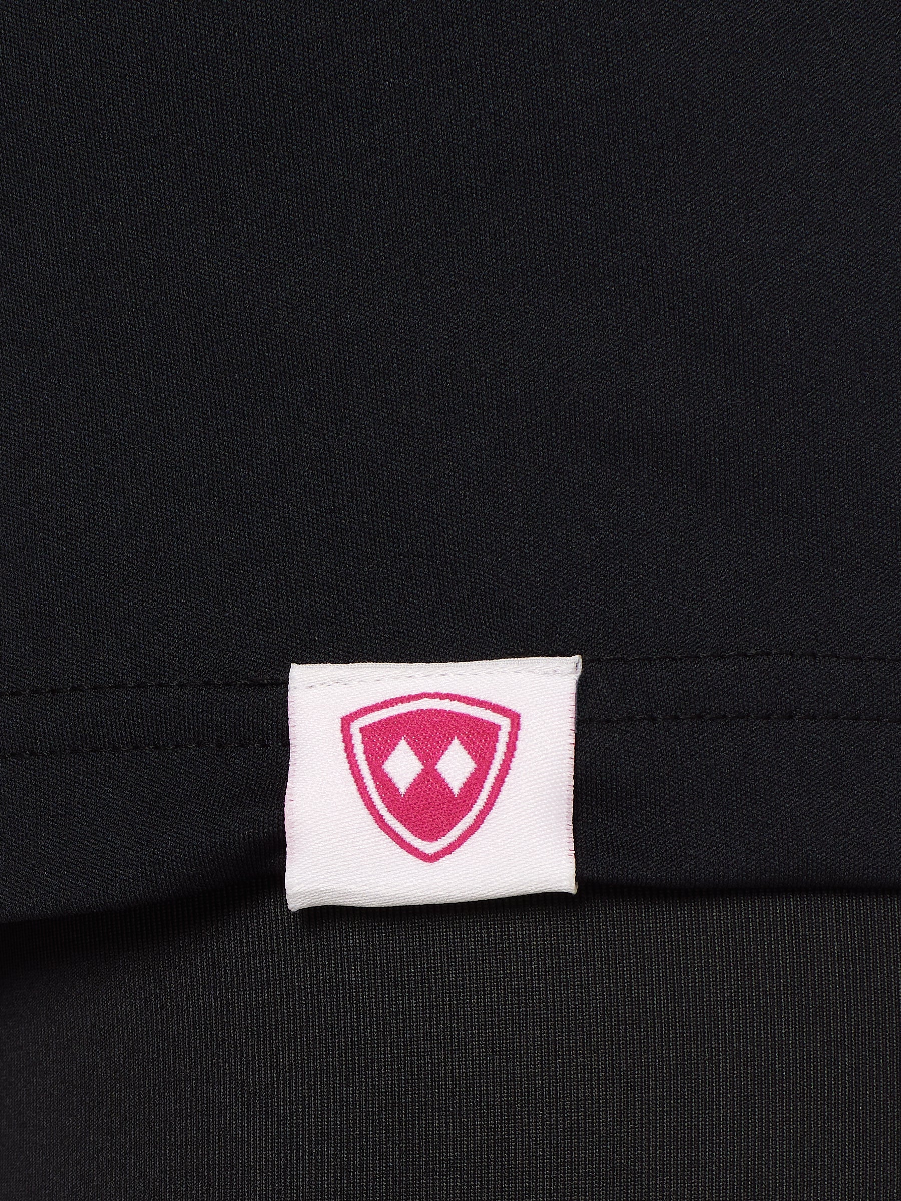 Close-up detail of a pink Double Diamond Shield woven hem label on a black performance long sleeve shirt.