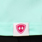 Close-up detail of a pink Double Diamond Shield woven hem label on a mint green performance long sleeve shirt.