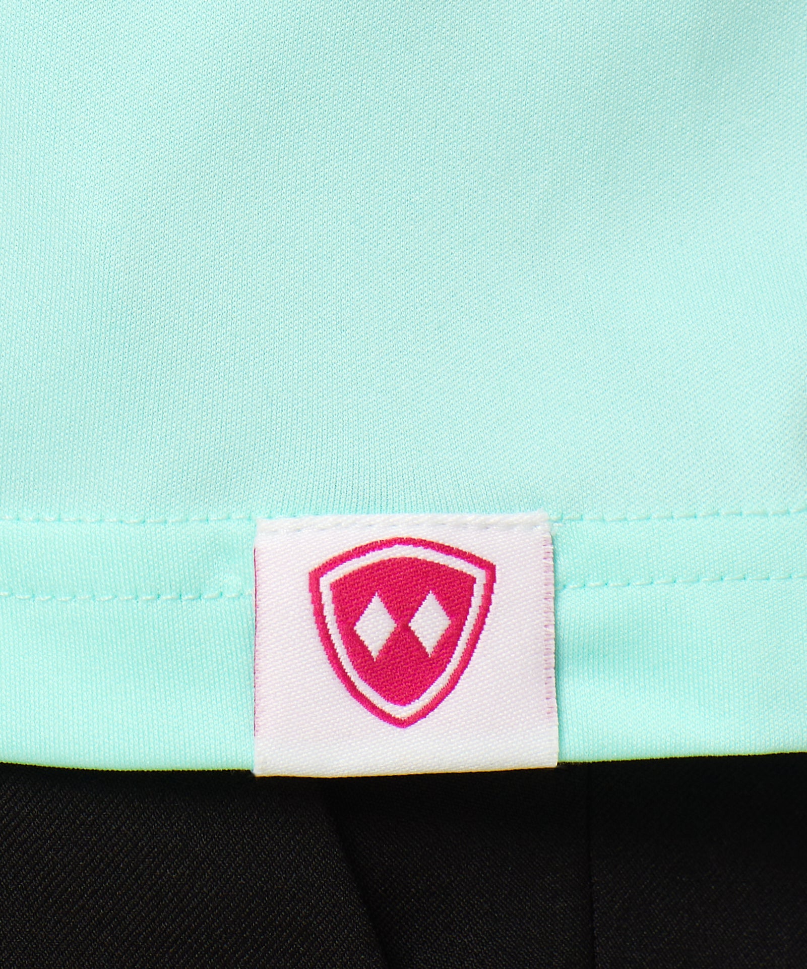 Close-up detail of a pink Double Diamond Shield woven hem label on a mint green performance long sleeve shirt.