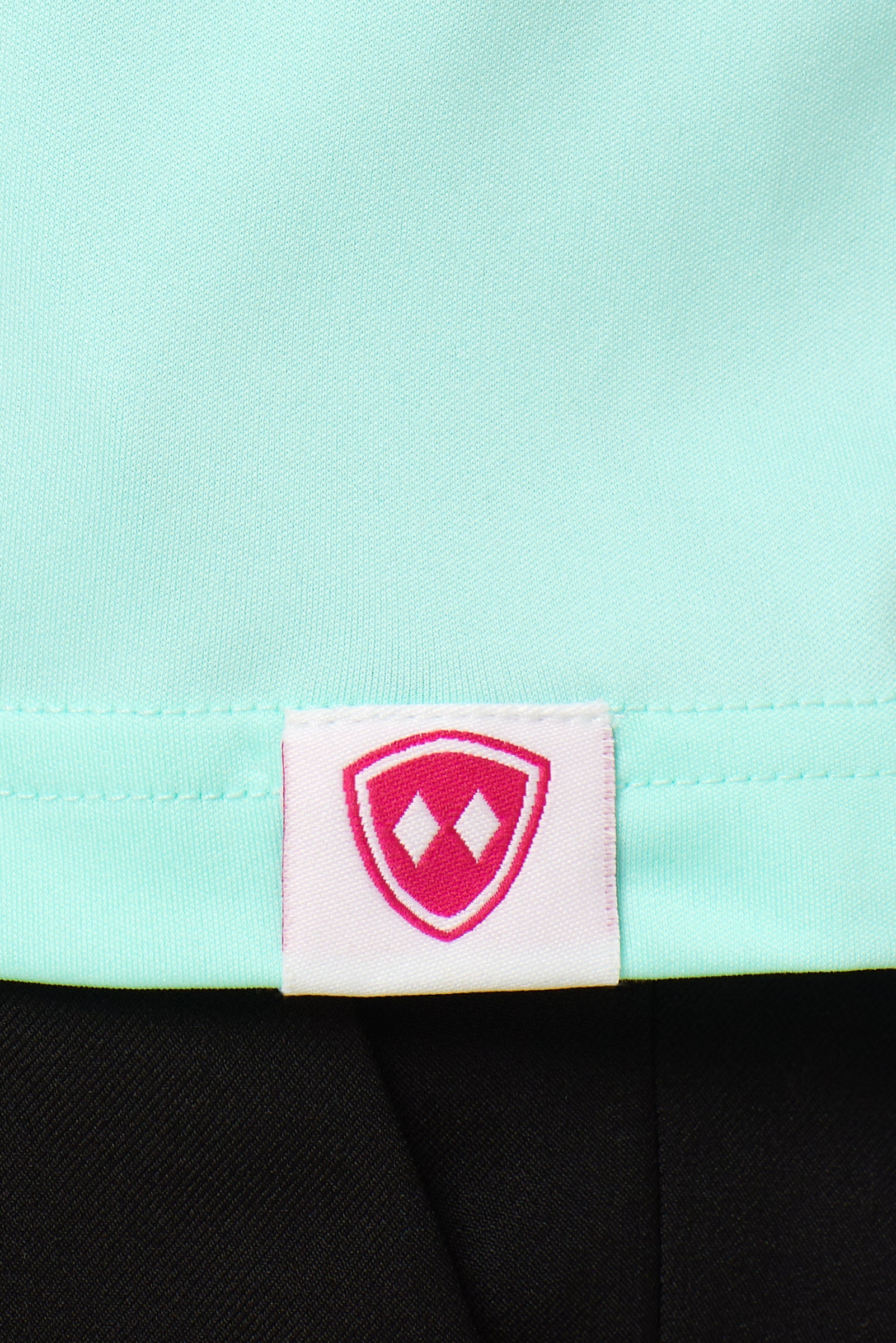 Close-up detail of a pink Double Diamond Shield woven hem label on a mint green performance long sleeve shirt.