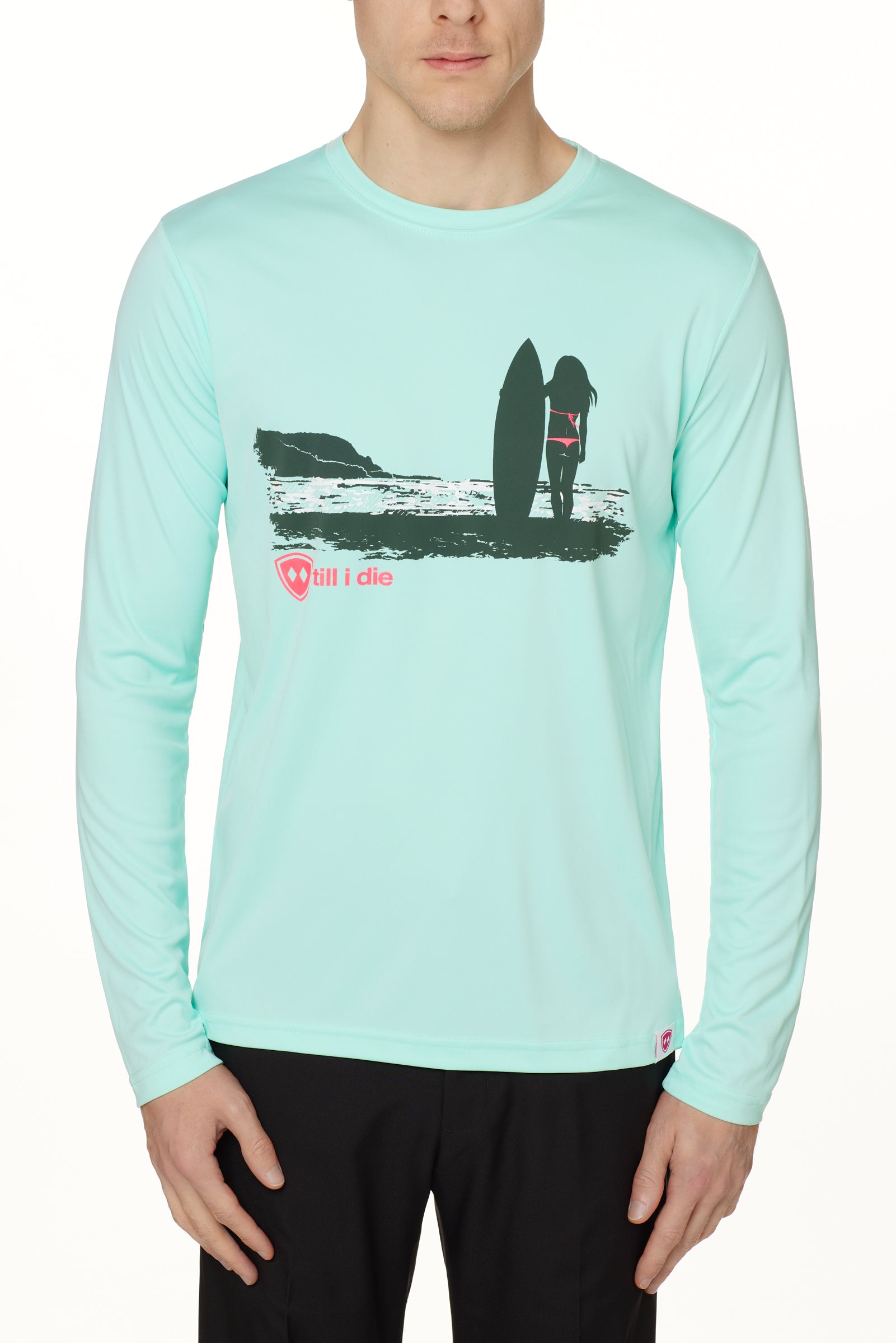 Front view of a male model wearing the Surf Girl long sleeve performance shirt in mint, shown on a white background. The graphic depicts a silhouetted female surfer standing with her board, gazing out at the ocean surf, with a hot pink “Till I Die” logo below the artwork.