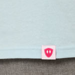 Close-up detail of a pink Double Diamond Shield woven hem label on a light blue tee shirt.