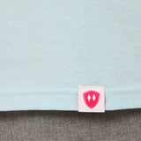 Close-up detail of a pink Double Diamond Shield woven hem label on a light blue tee shirt.