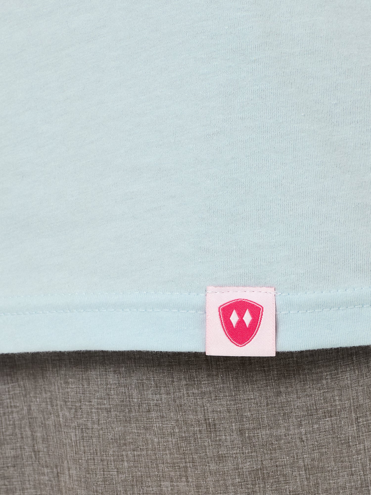Close-up detail of a pink Double Diamond Shield woven hem label on a light blue tee shirt.