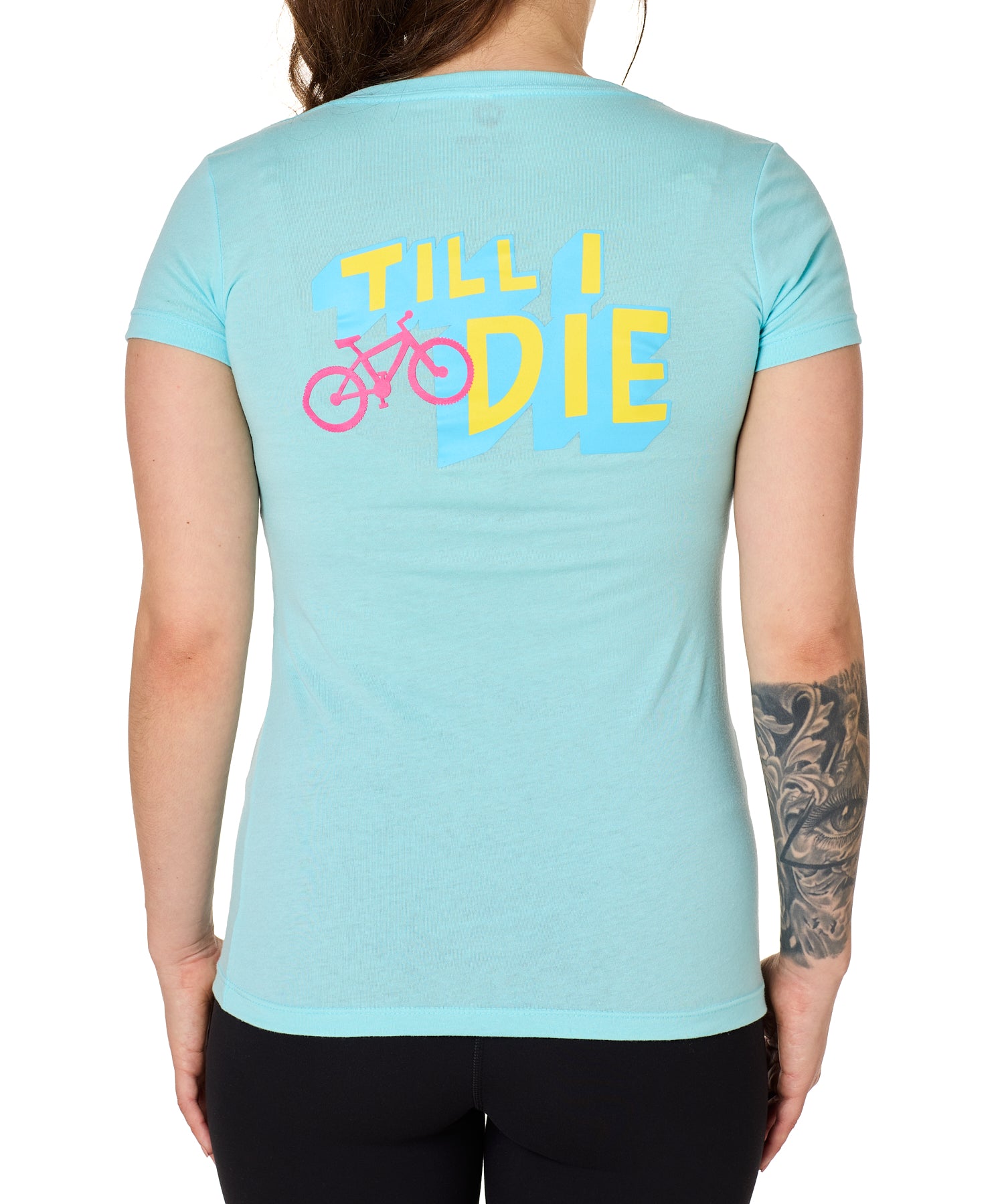 Back view of a female model wearing the Bike till i die tee shirt in cancun blue on a white background. The graphic features a pink mountain bike layered over bold blue and yellow till i die text