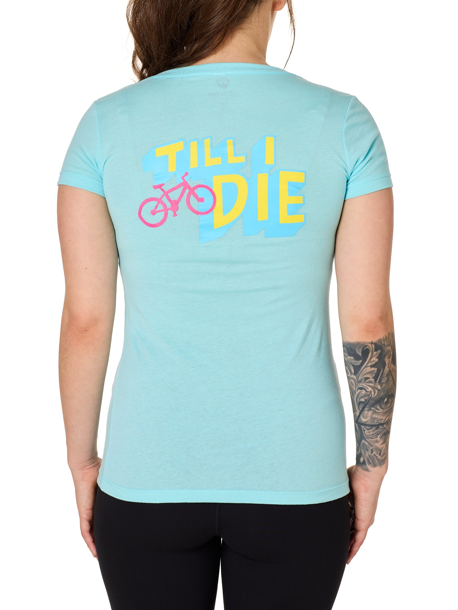 Back view of a female model wearing the Bike till i die tee shirt in cancun blue on a white background. The graphic features a pink mountain bike layered over bold blue and yellow till i die text