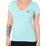 Front view of a female model wearing the Till I Die Bike V-Neck Tee in Cancun Blue on a white background. The shirt features a pink Double Diamond Shield logo on the wearer's left chest.