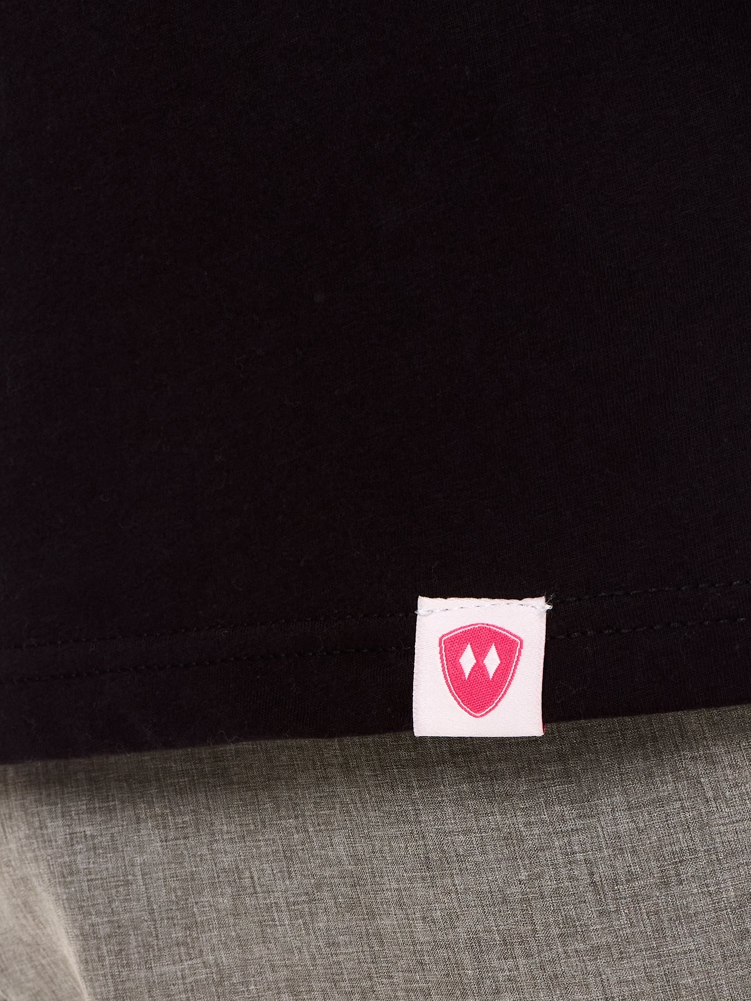 Close-up detail of a pink Double Diamond Shield woven hem label on a black shirt.
