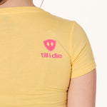 Back view of a female model wearing a Banana short sleeve shirt on a white background, featuring a hot pink Till I Die logo on the wearer’s top right shoulder.