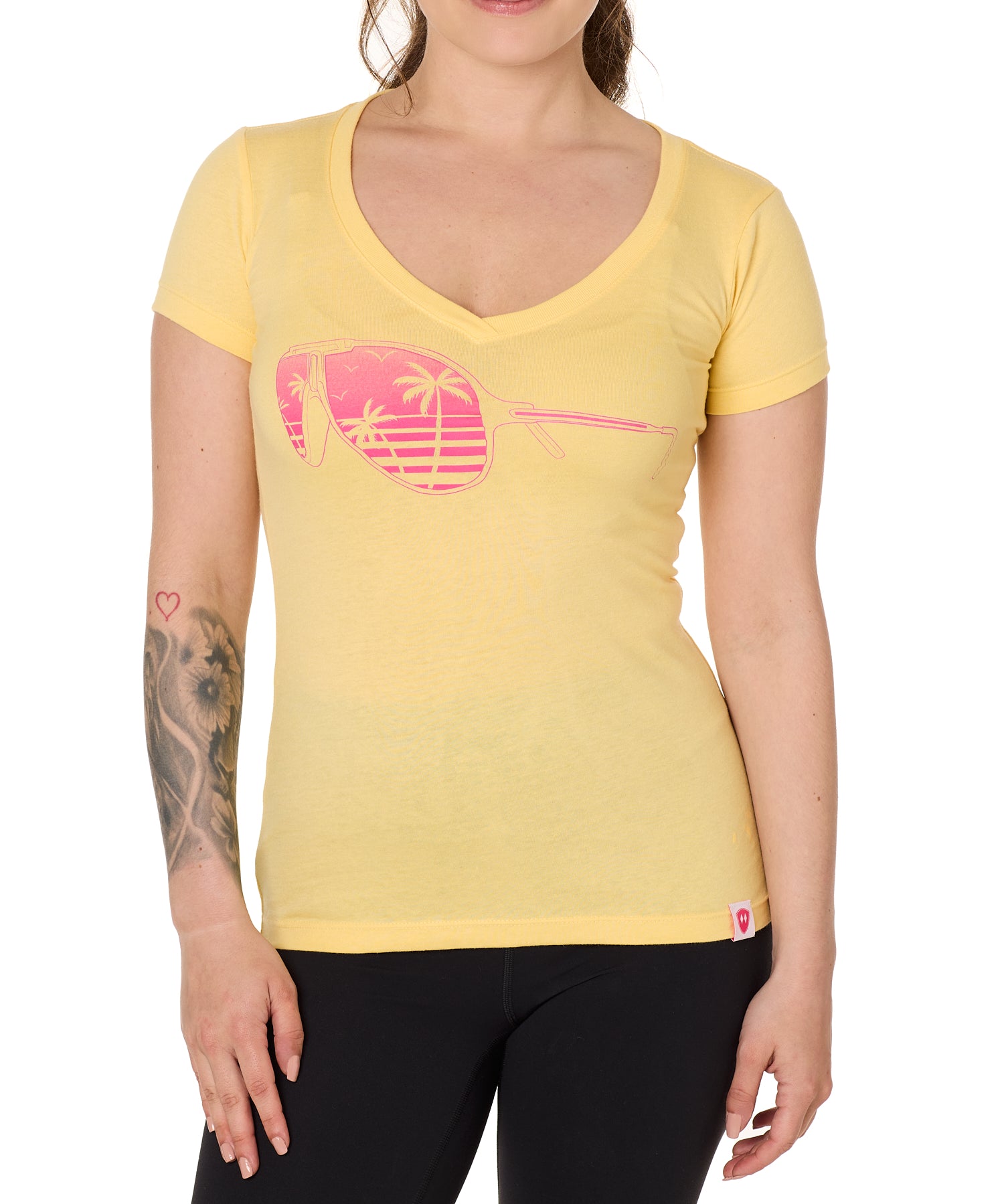 Front view of a female model wearing a short sleeve V neck Banana T-Shirt. The graphic features a pink print of sunglasses with a tropical beach scene reflected in the lenses.