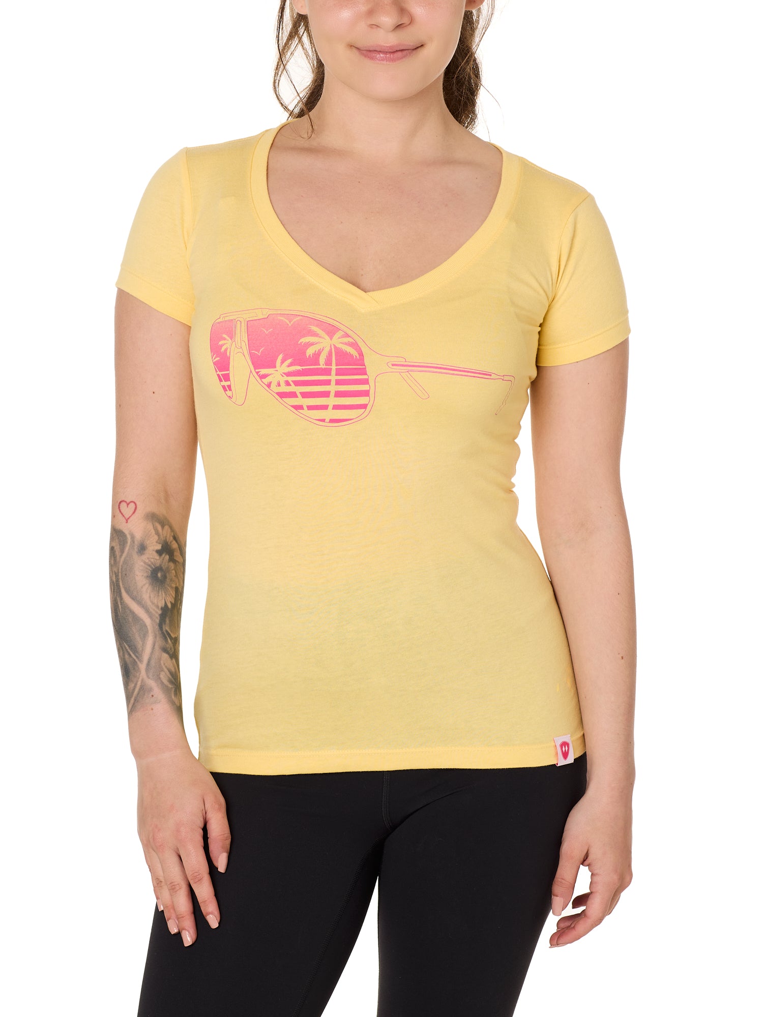 Front view of a female model wearing a short sleeve V neck Banana T-Shirt. The graphic features a pink print of sunglasses with a tropical beach scene reflected in the lenses.