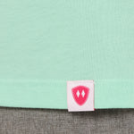 Close-up detail of a pink Double Diamond Shield woven hem label on a mint green shirt.