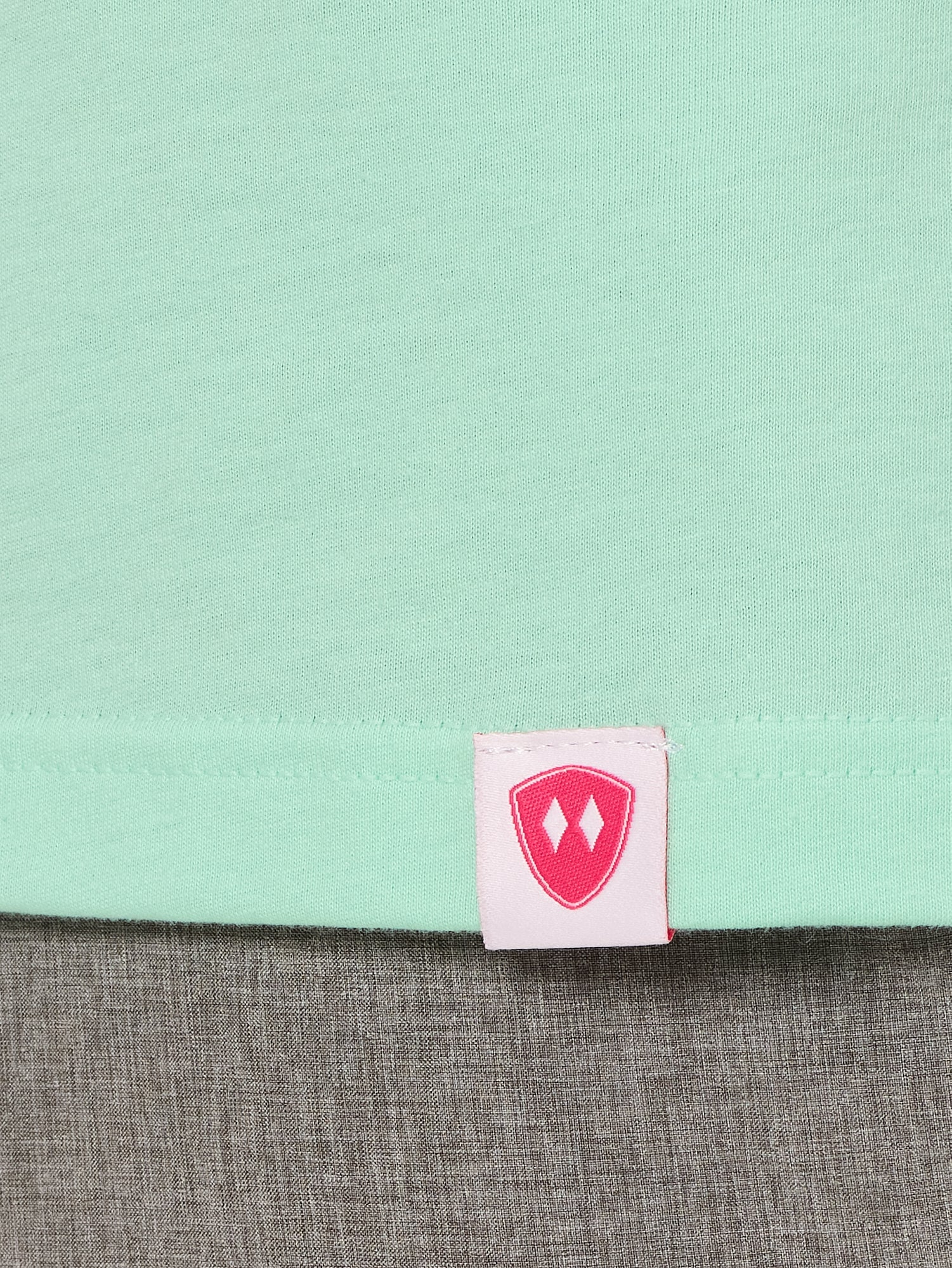 Close-up detail of a pink Double Diamond Shield woven hem label on a mint green shirt.