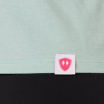 Close-up detail of a pink Double Diamond Shield woven hem label on a dusty blue tank.