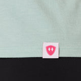Close-up detail of a pink Double Diamond Shield woven hem label on a dusty blue tank.