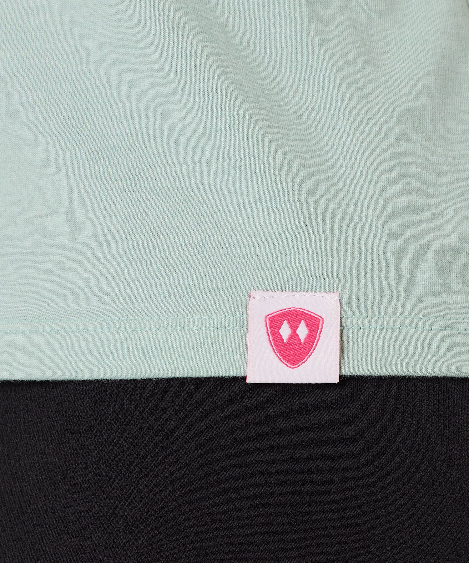 Close-up detail of a pink Double Diamond Shield woven hem label on a dusty blue tank.