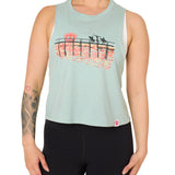 Front view of a female model wearing the Endless Summer tank in dusty blue, displayed on a white background. The graphic features three silhouetted surfers walking along an ocean boardwalk, with a setting sun—stylized as the Till I Die double diamond shield—glowing in the background.