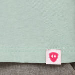 Close-up detail of a pink Double Diamond Shield woven hem label on a dusty blue crew neck tee.