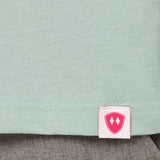 Close-up detail of a pink Double Diamond Shield woven hem label on a dusty blue crew neck tee.