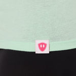 Close-up detail of a pink Double Diamond Shield woven hem label on a mint green v neck shirt.
