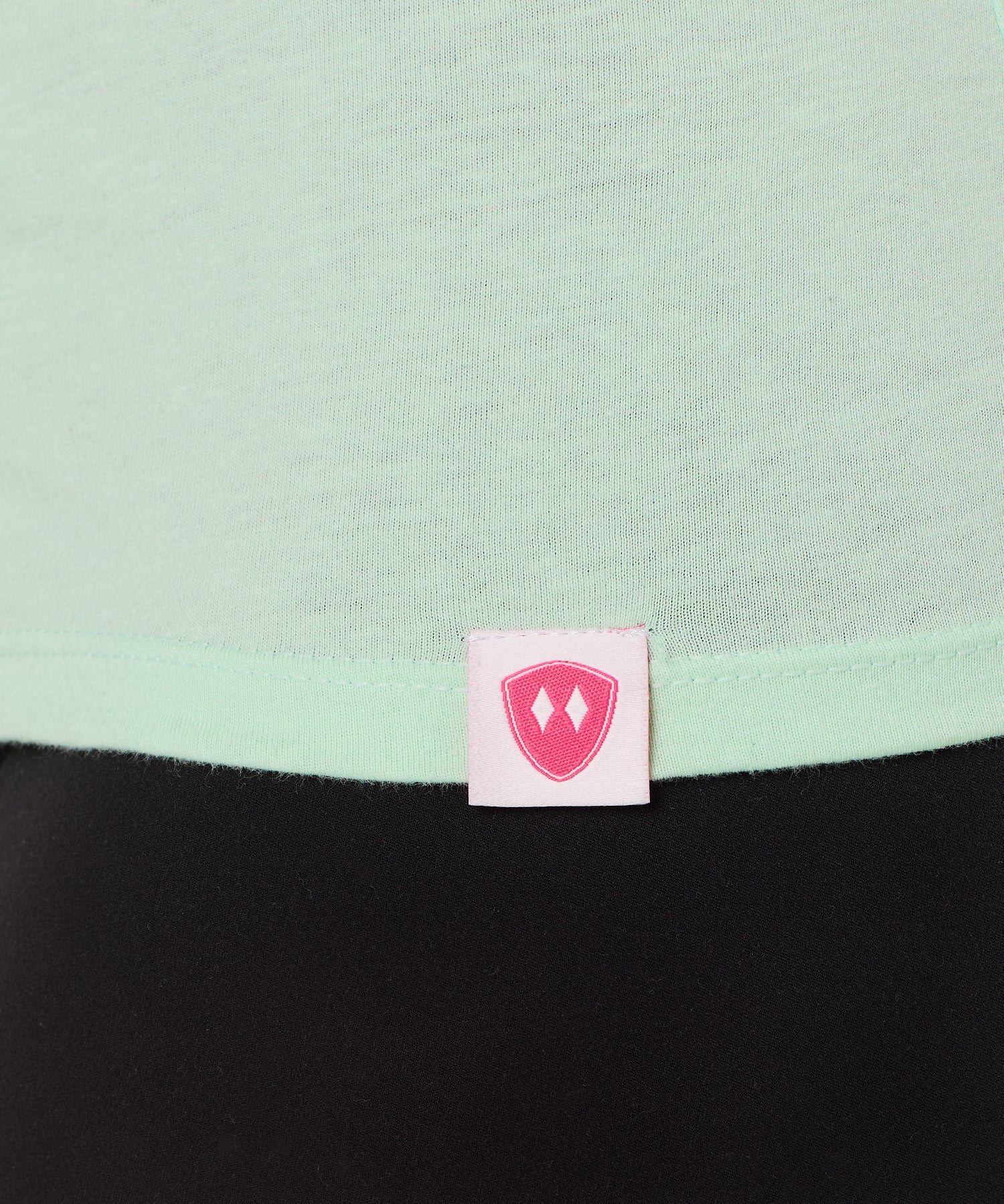 Close-up detail of a pink Double Diamond Shield woven hem label on a mint green v neck shirt.