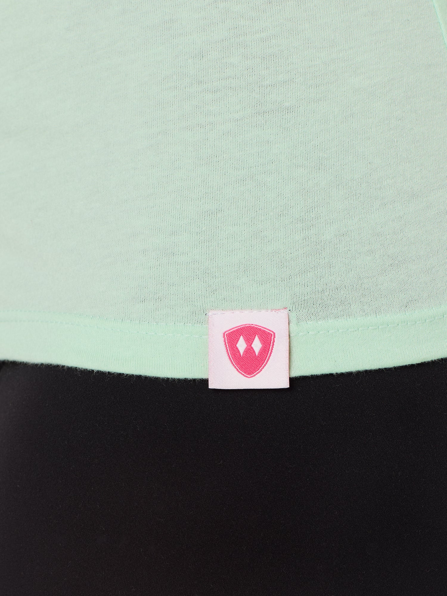 Close-up detail of a pink Double Diamond Shield woven hem label on a mint green v neck shirt.