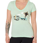 Front view of a female model wearing the Hammock V-neck tee in mint, displayed on a white background. The graphic depicts a vintage VW bus parked on a beach, with a surfboard leaning against it and a silhouetted figure relaxing in a hammock strung between the van and a palm tree.